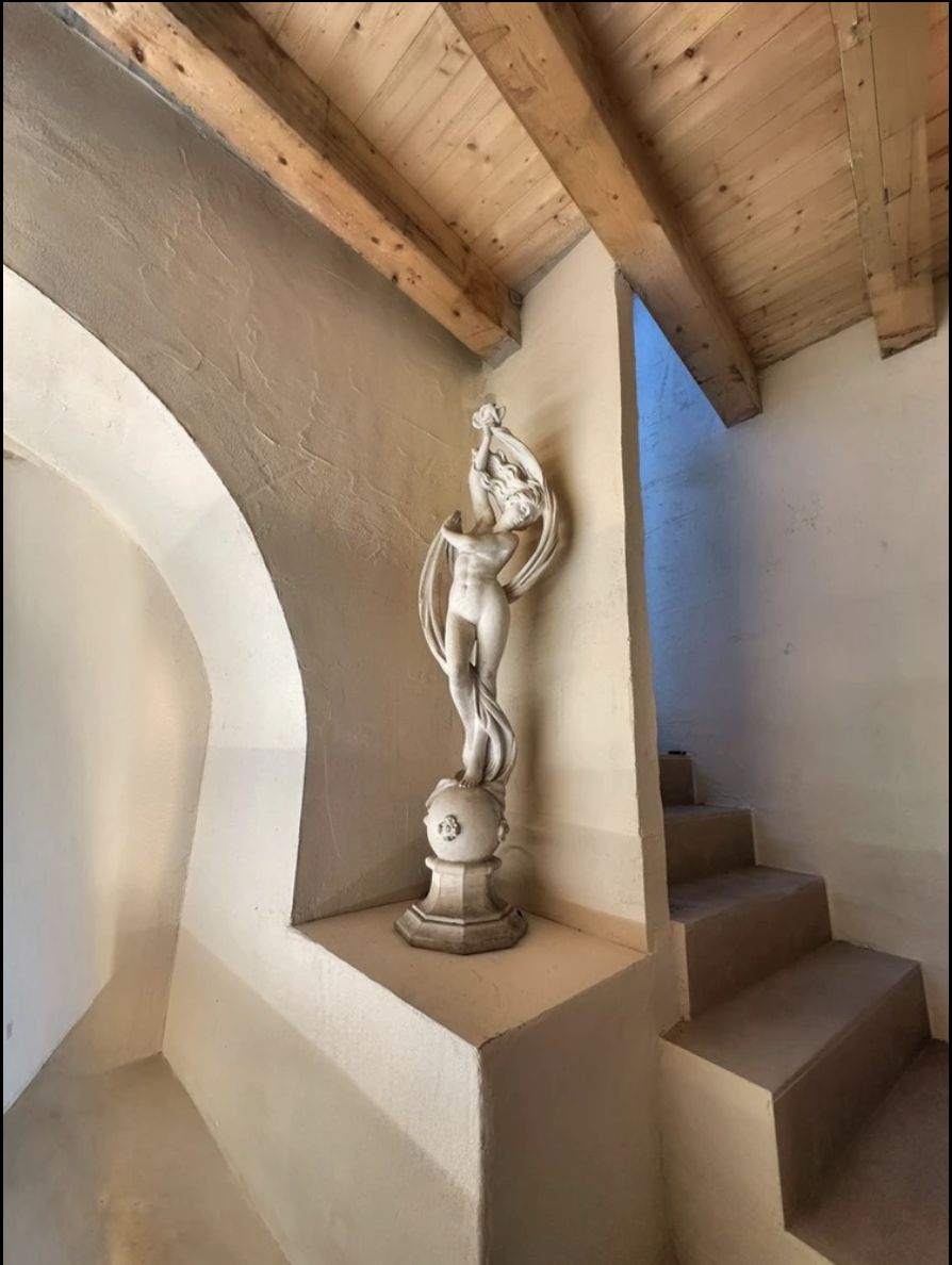 Una statua femminile scolpita in una nicchia intonacata, sotto un soffitto con travi di legno a vista.
