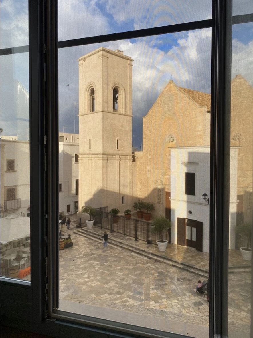 Vista da una finestra del palazzo sulla piazza, verso il campanile in pietra e la chiesa di Polignano a Mare.