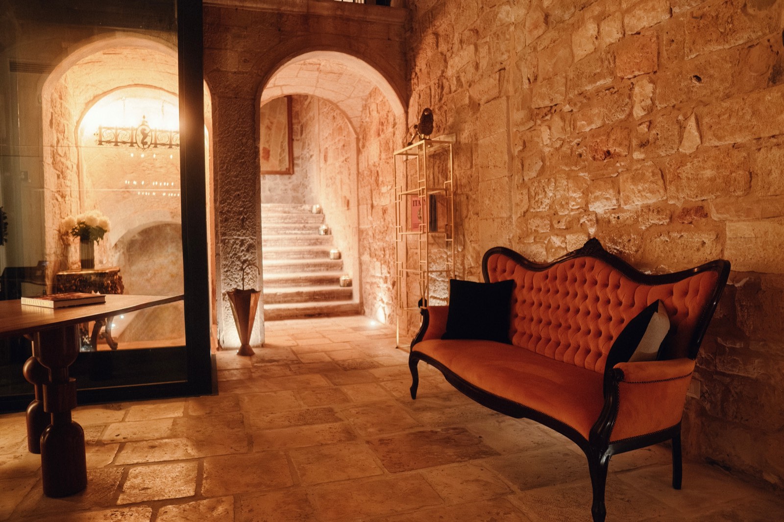A coral velvet sofa against the stone wall of the entrance, with an archway opening onto the original stone staircase.