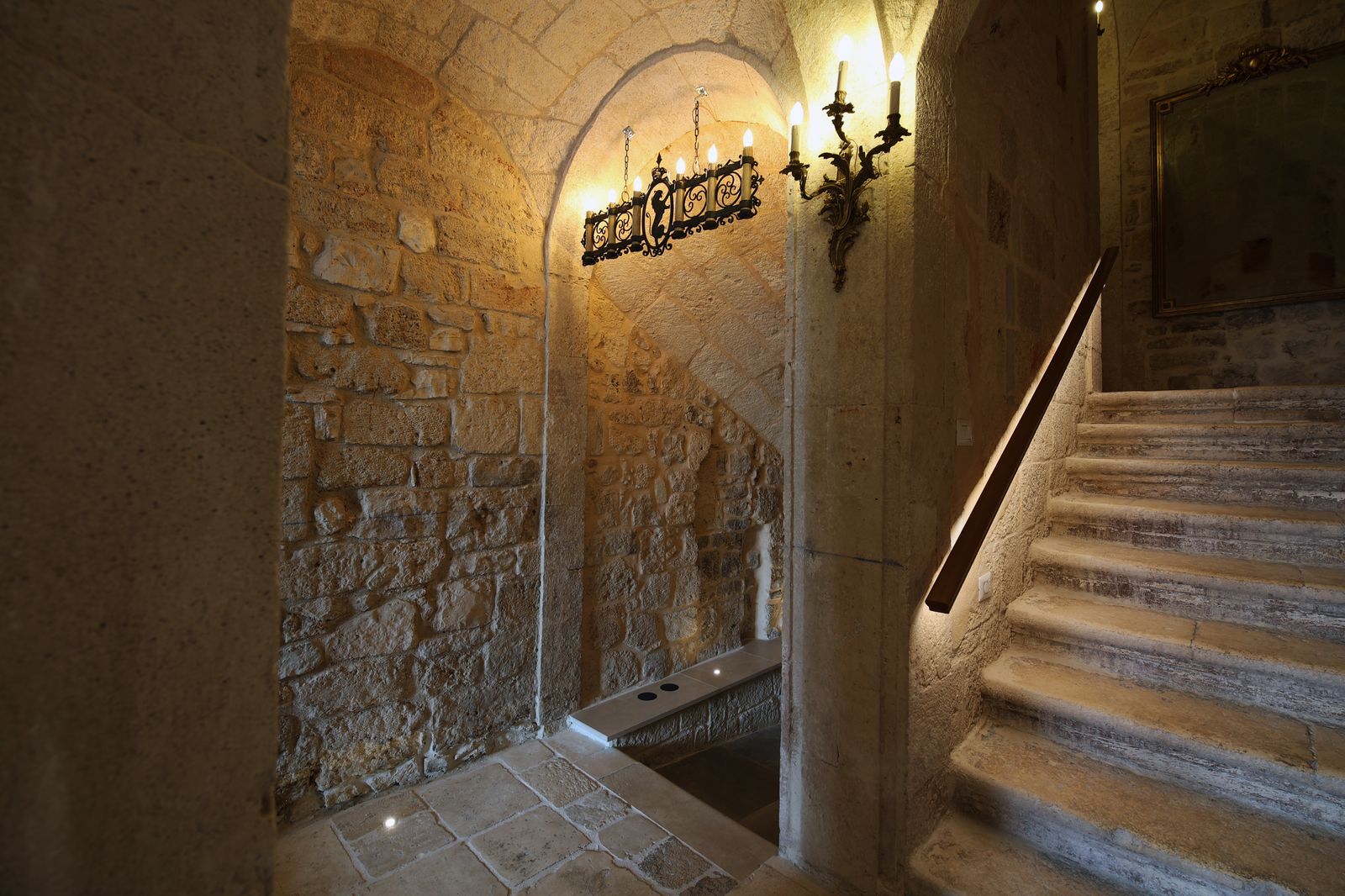 La scala originale in pietra del palazzo, illuminata da un lampadario in ferro battuto e da un'applique dorata.
