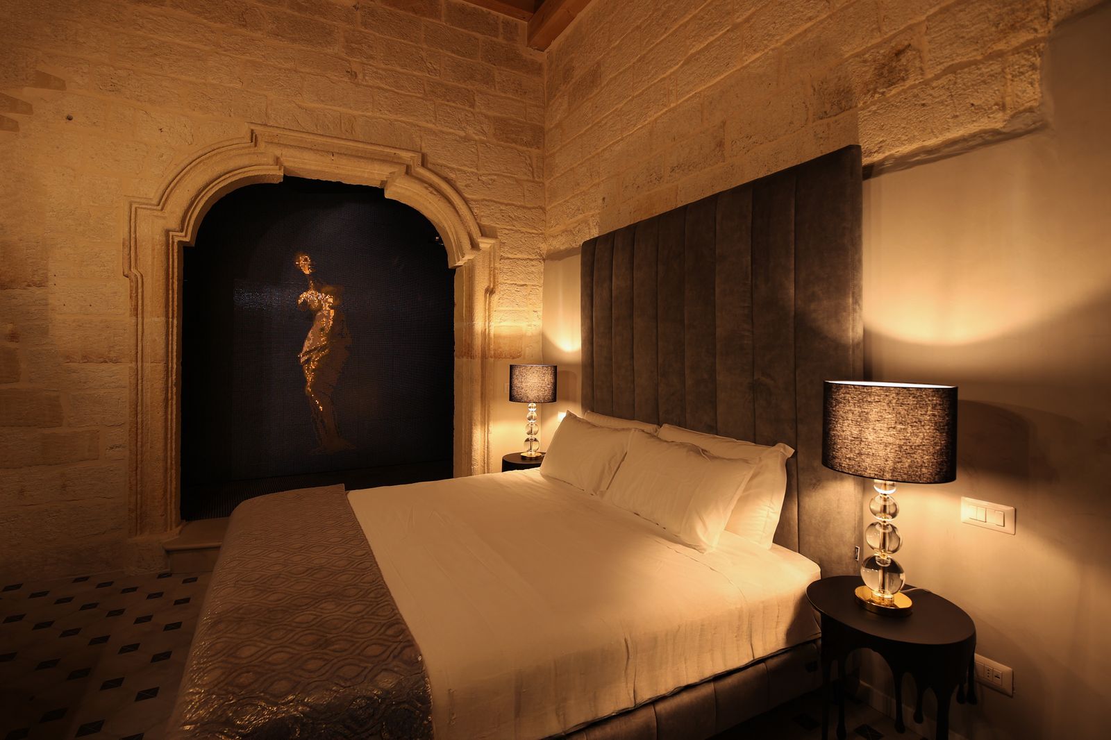 Camera con pareti in pietra a vista e una figura di Venere retroilluminata in una nicchia scolpita dietro il letto.