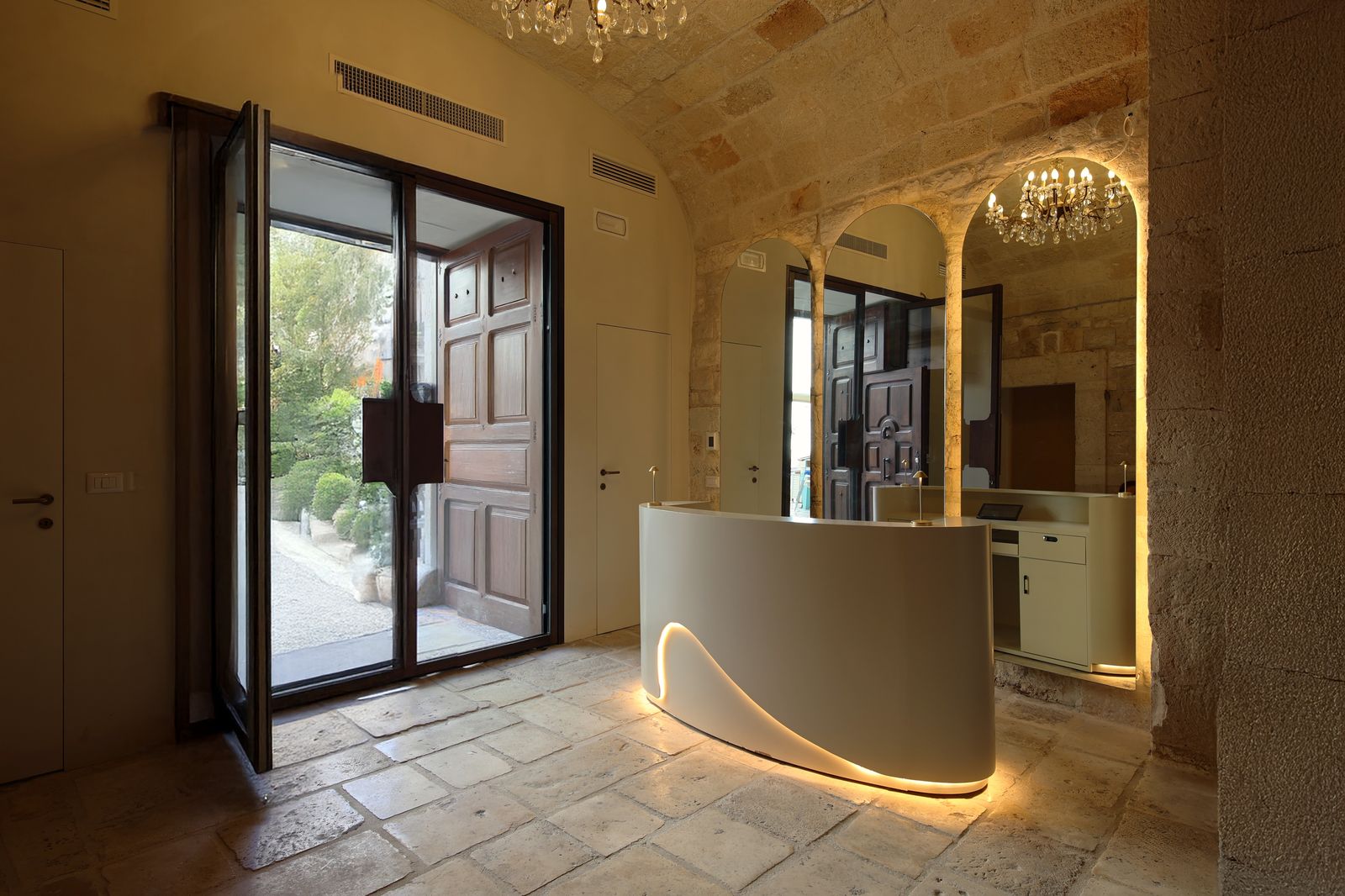 La lobby d'arrivo di The Duchess of Puglia, con bancone curvo della reception, specchi ad arco e volta in pietra.