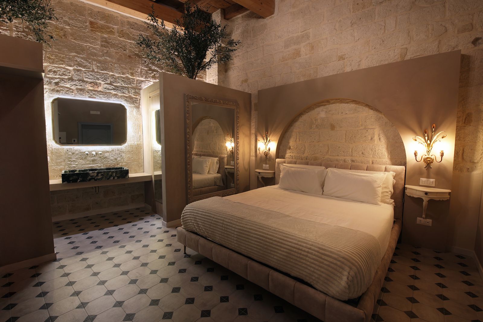 Garden Deluxe Room: letto in una nicchia di pietra ad arco, lavabo in marmo verde e un ulivo sotto il soffitto con travi in legno.
