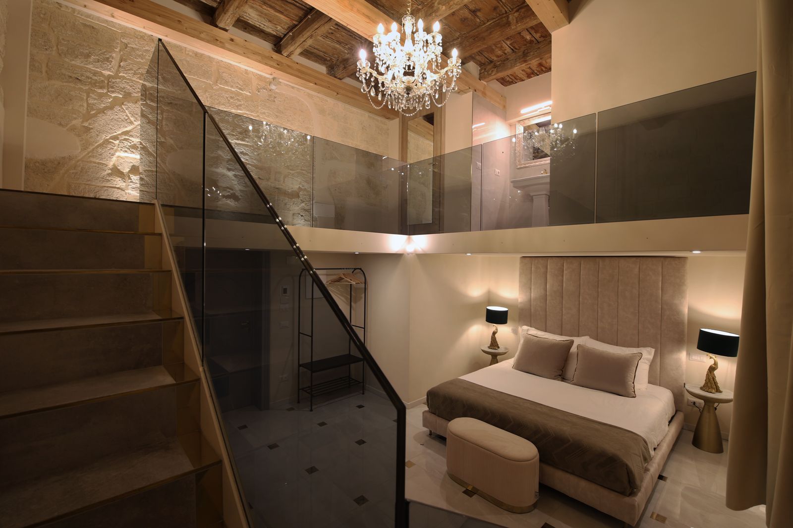 Reflection Junior Suite: ambiente a doppia altezza con lampadario di cristallo appeso al soffitto a travi originale e scala che sale al soppalco.