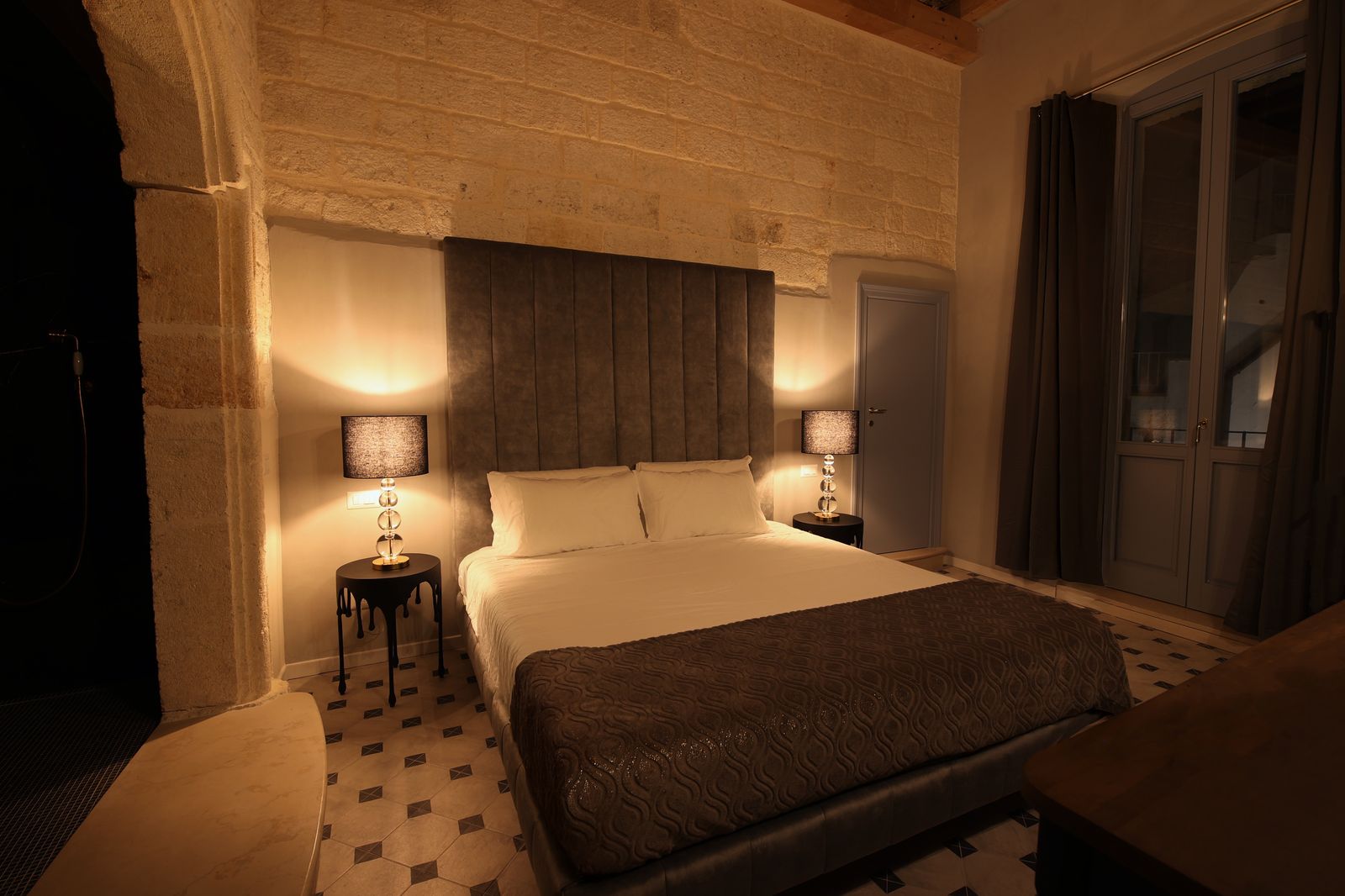 Venus Deluxe Room: letto contro la pietra a vista sotto un soffitto alto, con un'apertura ad arco in pietra verso il bagno.