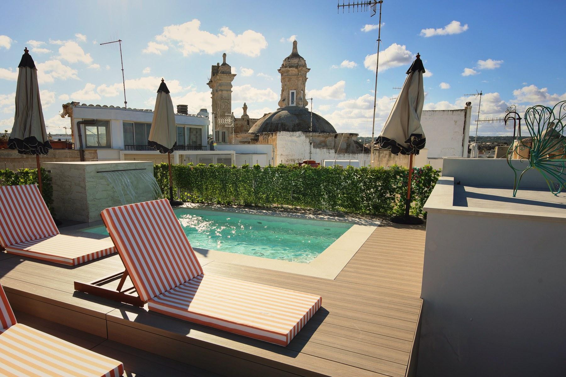 Lettini a righe e ombrelloni intorno alla piscina riscaldata sul tetto, con la cupola e il campanile di Polignano sullo sfondo.