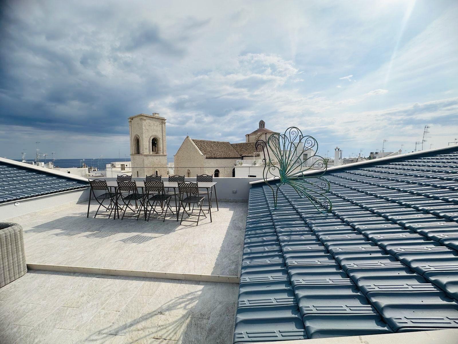 Un lungo tavolo apparecchiato sulla terrazza sul tetto, di fronte al campanile, alla chiesa e al mare di Polignano.