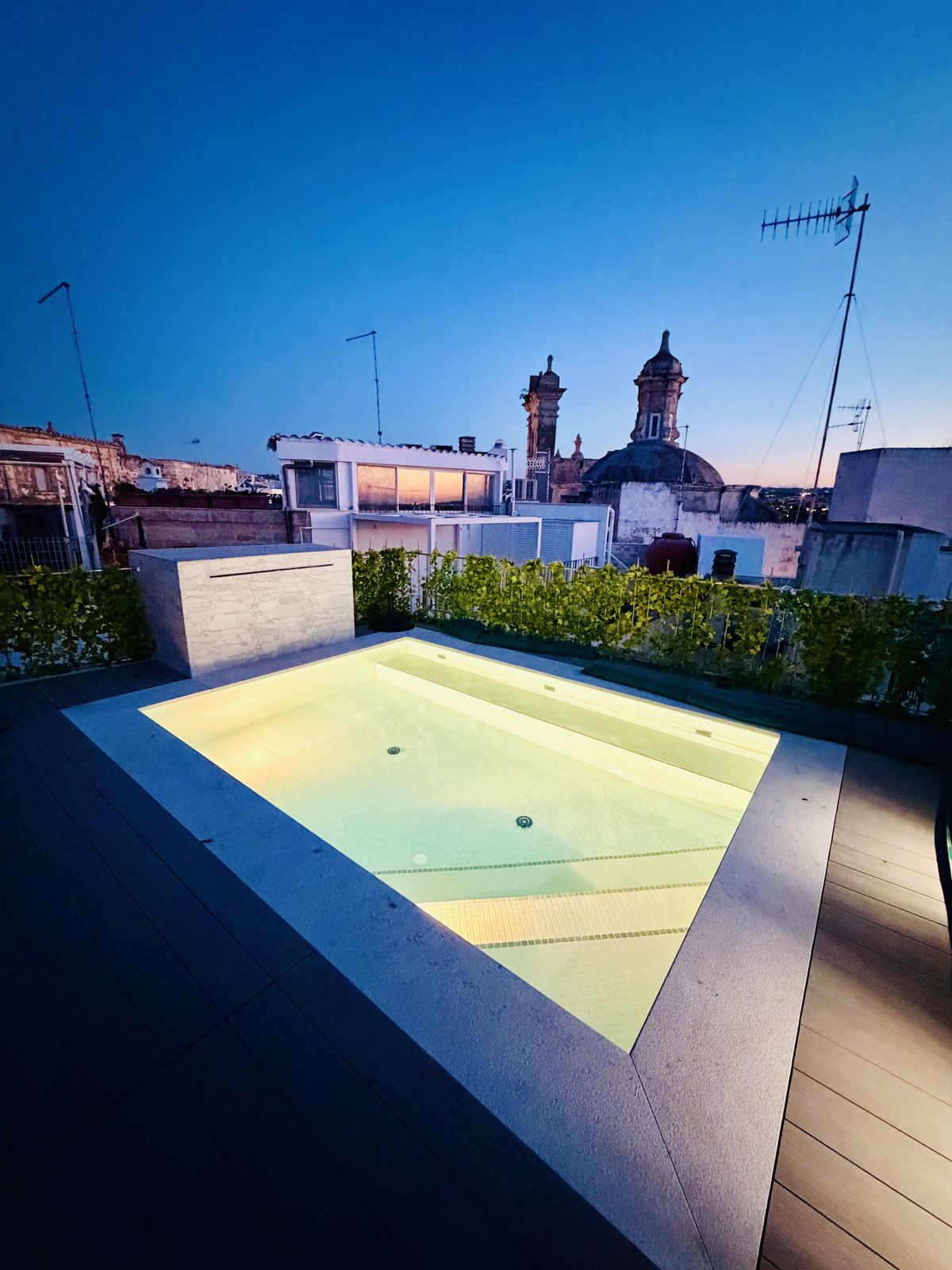 La piscina sul tetto illuminata al crepuscolo, con le cupole del centro storico di Polignano contro un cielo blu intenso.